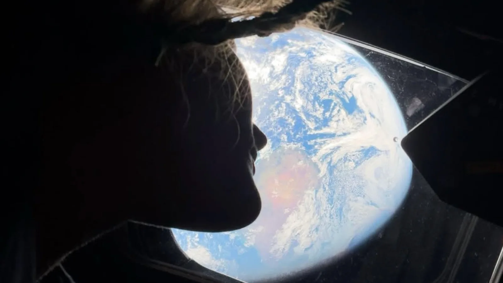 Astronaut privind spre Pământ printr-o fereastră a navei spațiale.