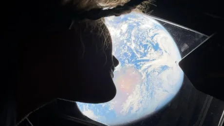 Astronaut privind spre Pământ printr-o fereastră a navei spațiale.
