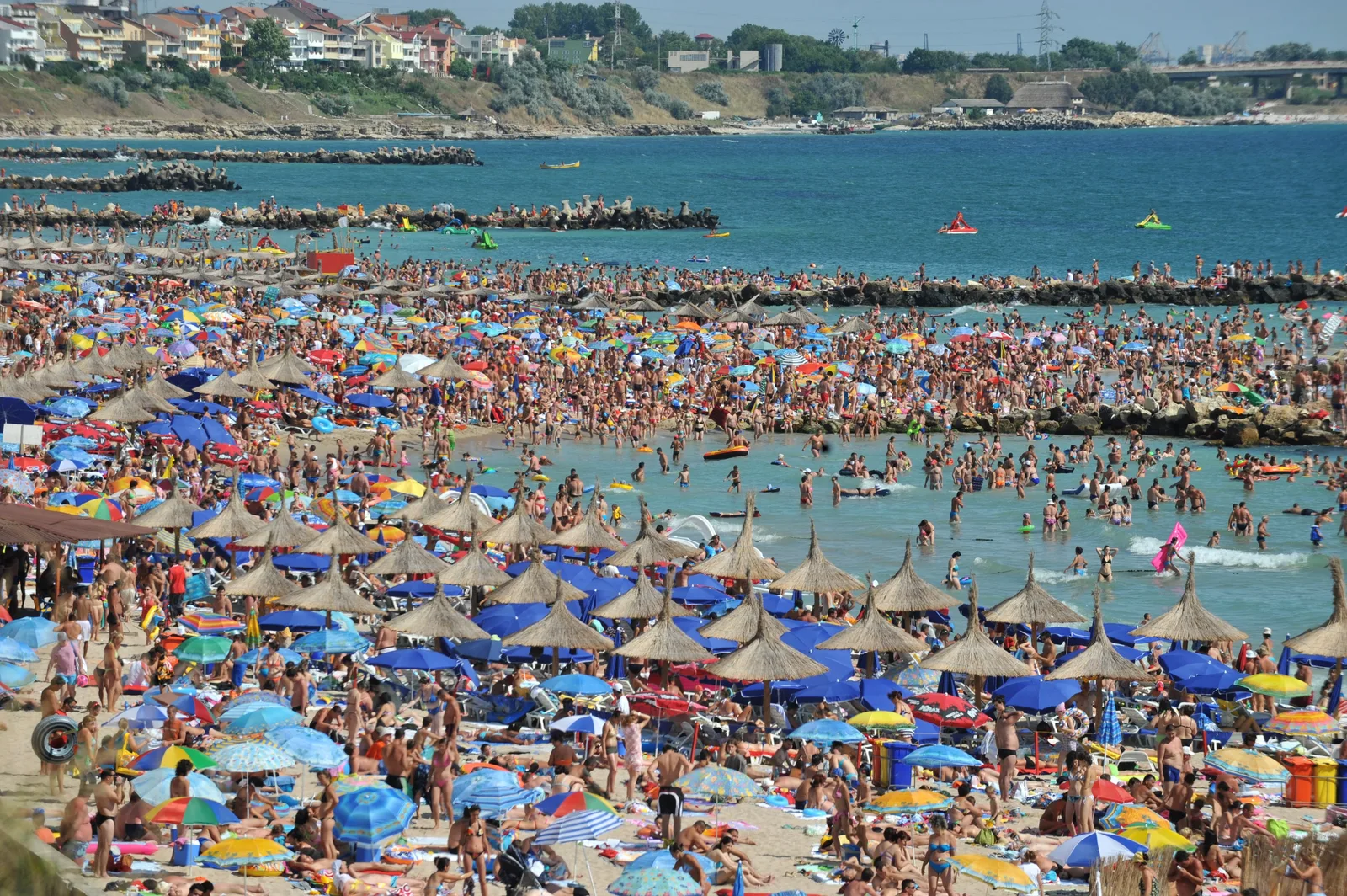 Plajă aglomerată pe litoralul românesc, cu umbrele colorate și turiști.