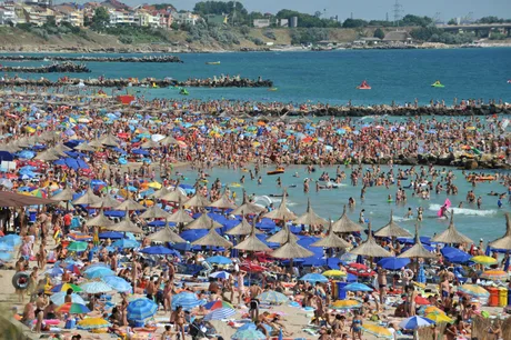Plajă aglomerată pe litoralul românesc, cu umbrele colorate și turiști.