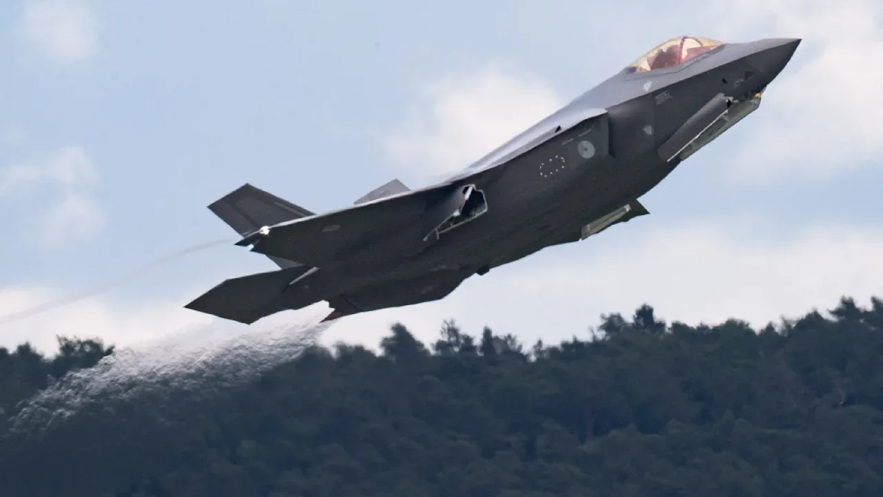 Un avion F-35 decolând, înconjurat de peisaj montan verde.