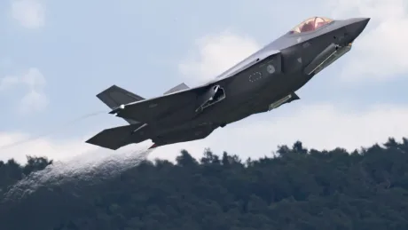 Un avion F-35 decolând, înconjurat de peisaj montan verde.