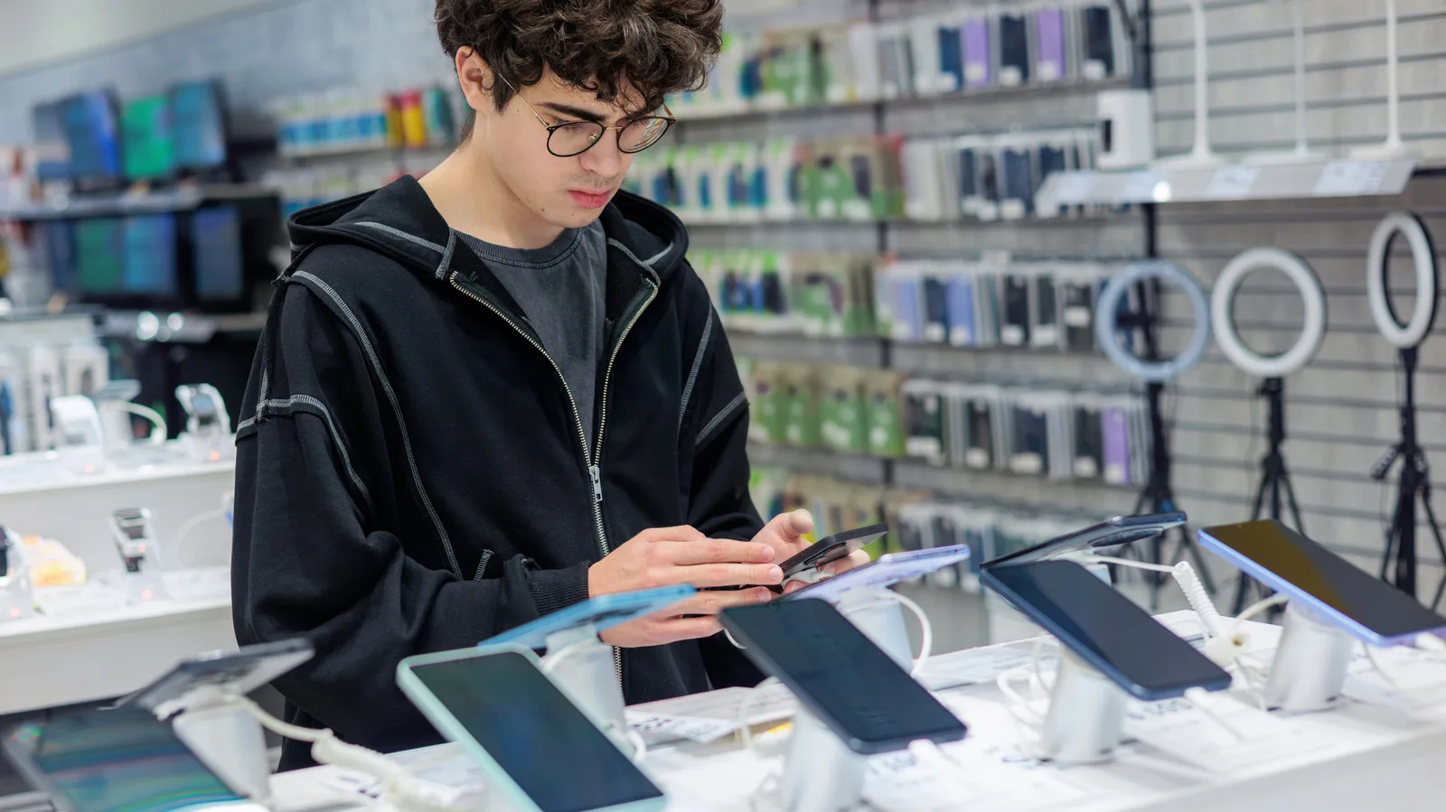 Un tânăr analizează gadgeturi într-un magazin de tehnologie.