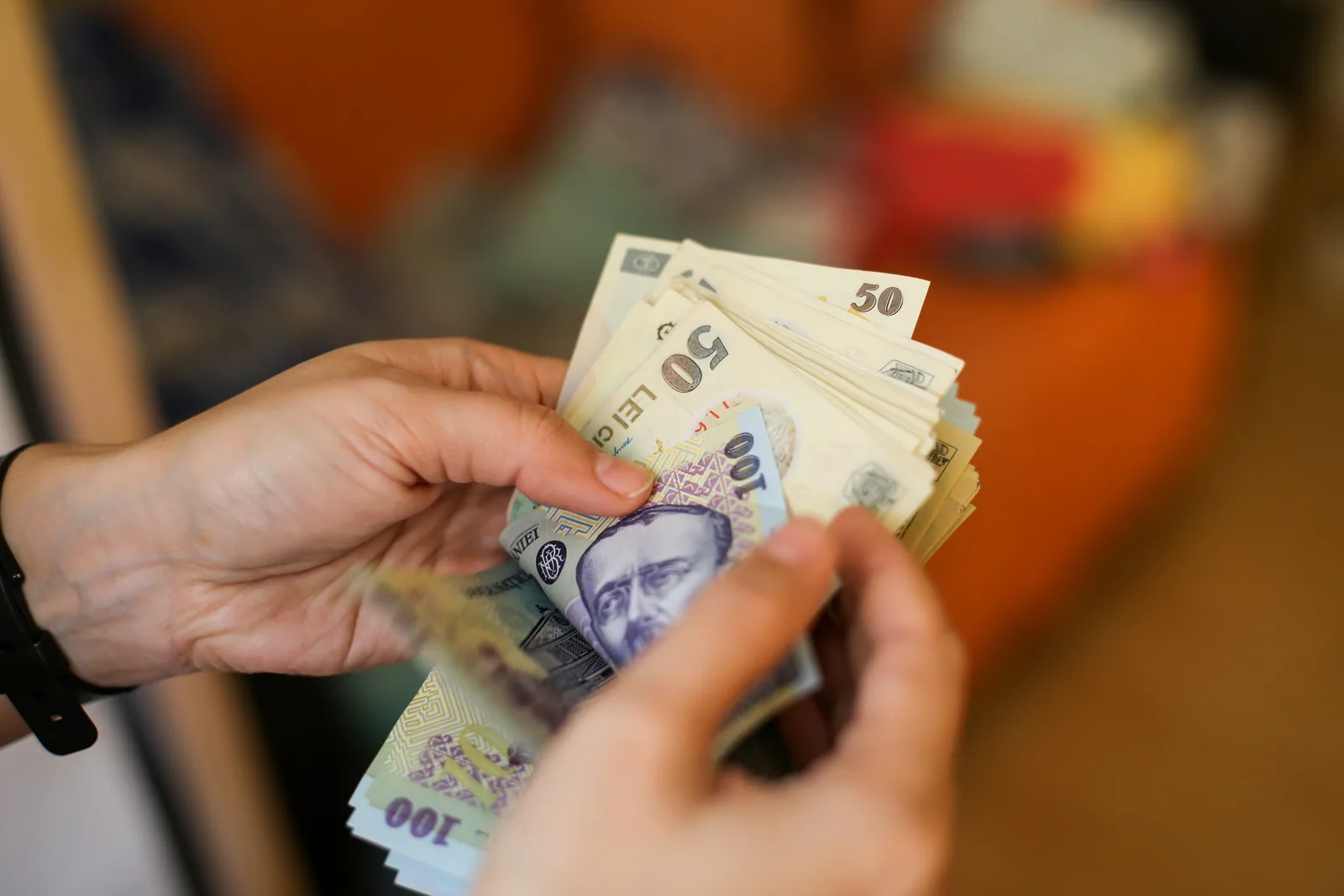 Bancnote românești numărate de o persoană în interiorul unei camere.