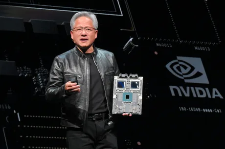 Jensen Huang prezentând o placă de bază pe scenă, purtând o geacă de piele neagră.