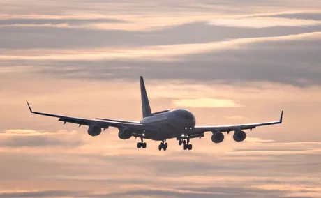Aeronave în apropierea unui aeroport, cu cerul colorat la apus.