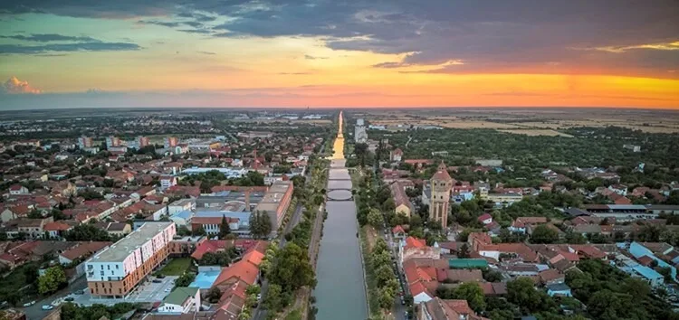 Vedere panoramică a malului Begăi la apus, cu clădiri și vegetație.
