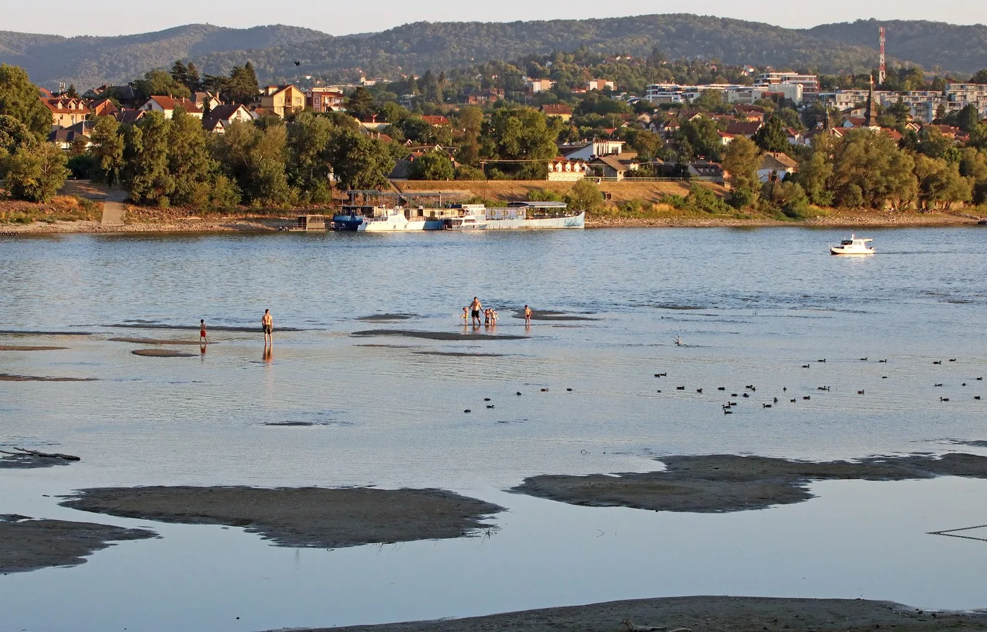 Peisaj fluvial cu oameni pe malul Dunării în timpul secetei.