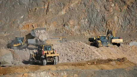 Utilaje grele extrag minerale dintr-o carieră de piatră.