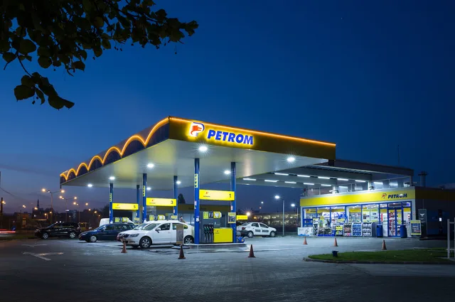 Stație de alimentare Petrom iluminată noaptea, cu mașini parcate.
