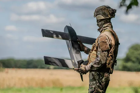 Un soldat ținând o dronă militară în peisajul natural.