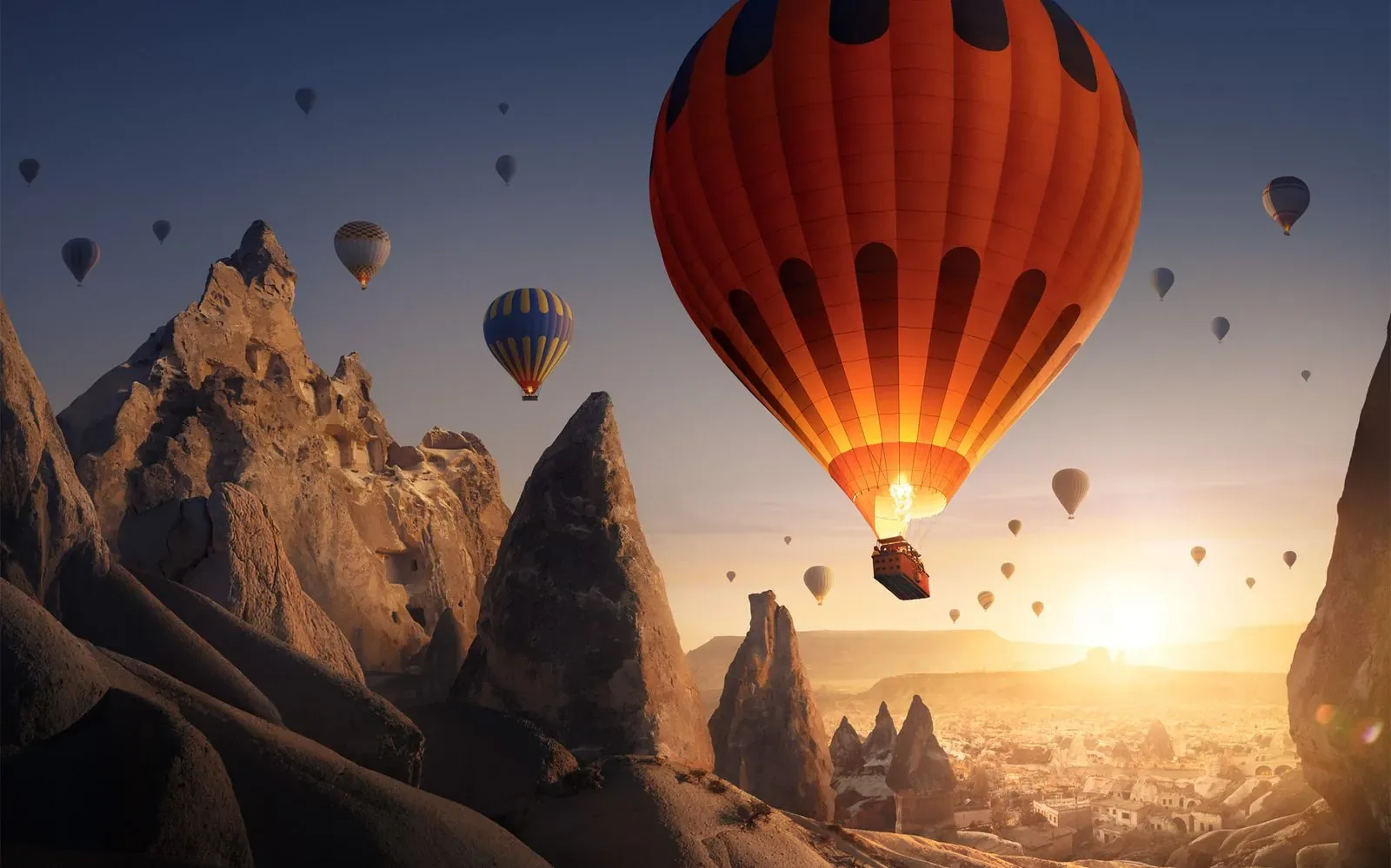 Balon cu aer cald zburând deasupra unui peisaj montan la apus.
