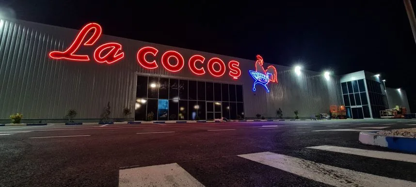 Fasada magazinului La Cocoș iluminată noaptea, cu logo-ul vizibil.
