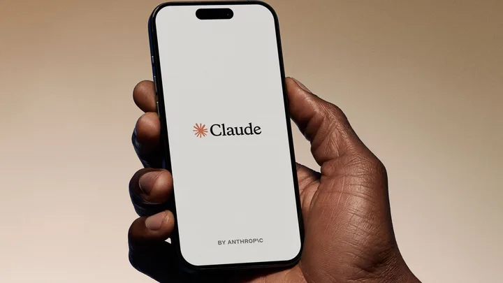 Un telefon mobil cu logo-ul Claude pe ecran, ținut de o mână.