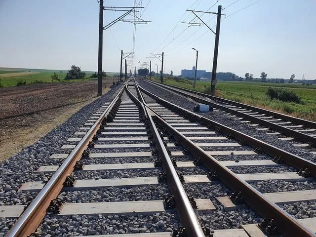Tronson feroviar în apropierea unei zone agricole, cu linii ce se bifurcă.