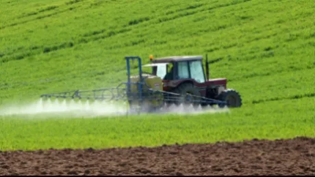 Tractor pe câmp, aplicând tratamente agricole pe o suprafață verde.