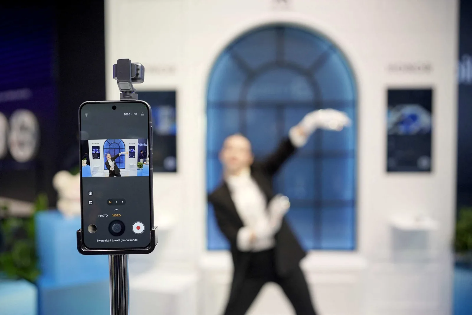 Un smartphone pe un suport, cu un fundal elegant și o persoană blurată în spate.