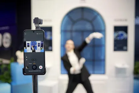 Un smartphone pe un suport, cu un fundal elegant și o persoană blurată în spate.