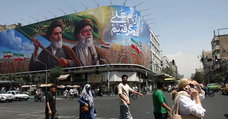 Oameni traversând o stradă aglomerată, cu un mural pe fundal în Teheran.
