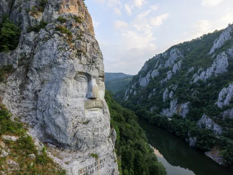 Statuia lui Decebal sculptată în stâncă, pe malul Dunării, înconjurată de peisaje montane verzi.
