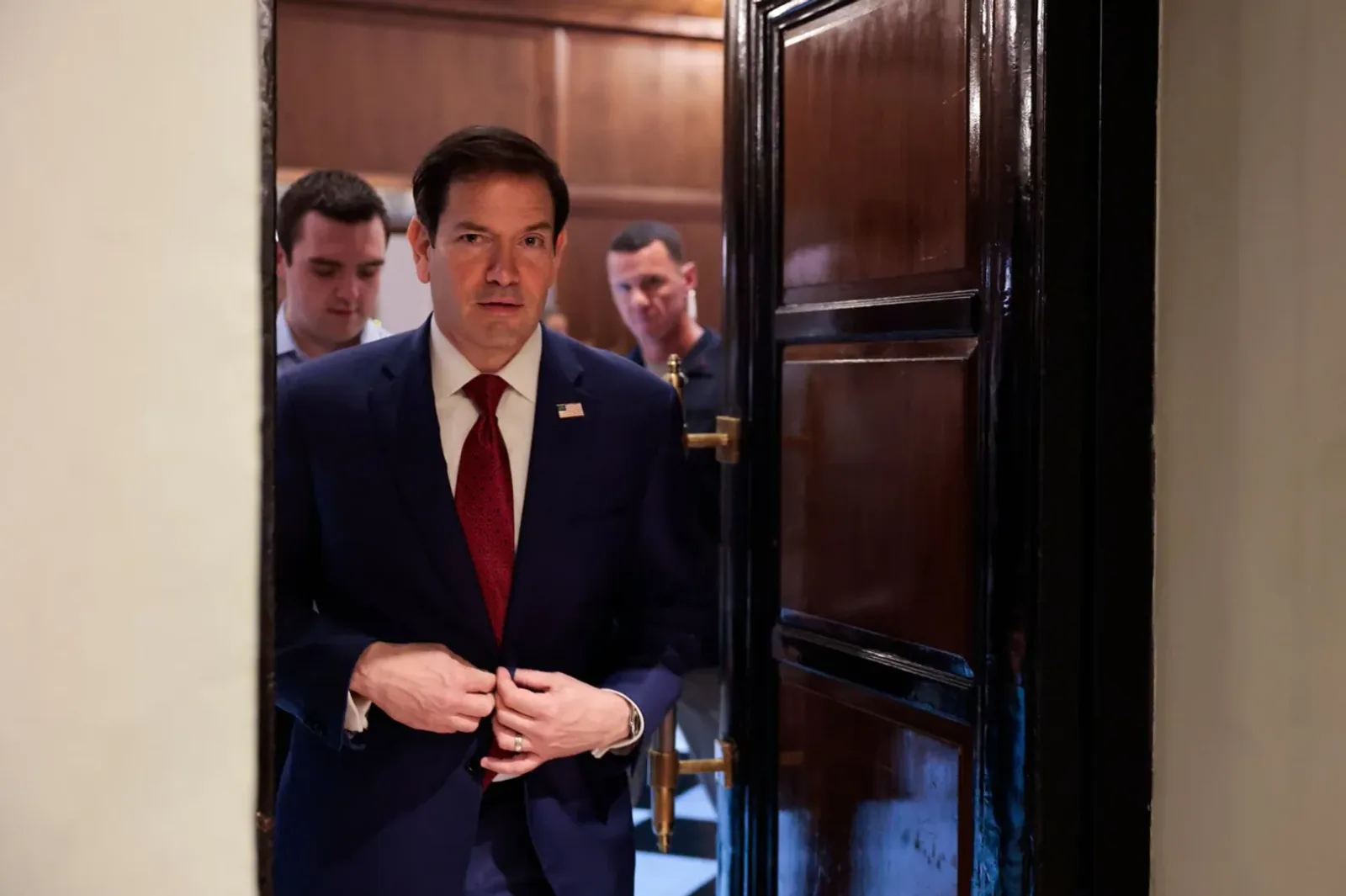 Marco Rubio intrând într-o încăpere, purtând un costum elegant.
