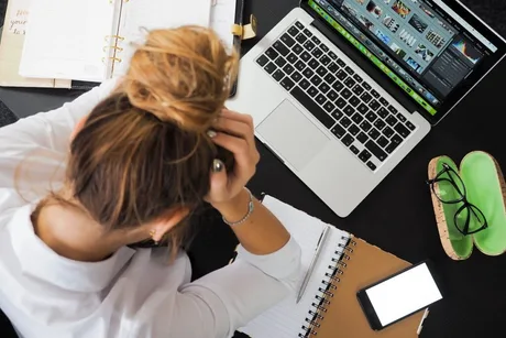 O persoană îngrijorată lucrând la laptop, cu notițe și telefon pe birou.