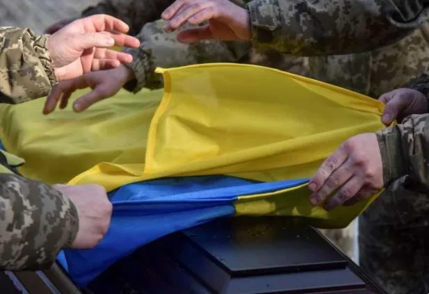 Soldați ucraineni acoperind un sicriu cu steagul național.