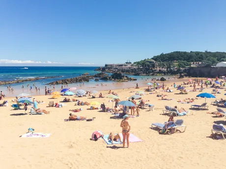 Plajă aglomerată din Sicilia, turiști relaxându-se sub umbrele colorate.
