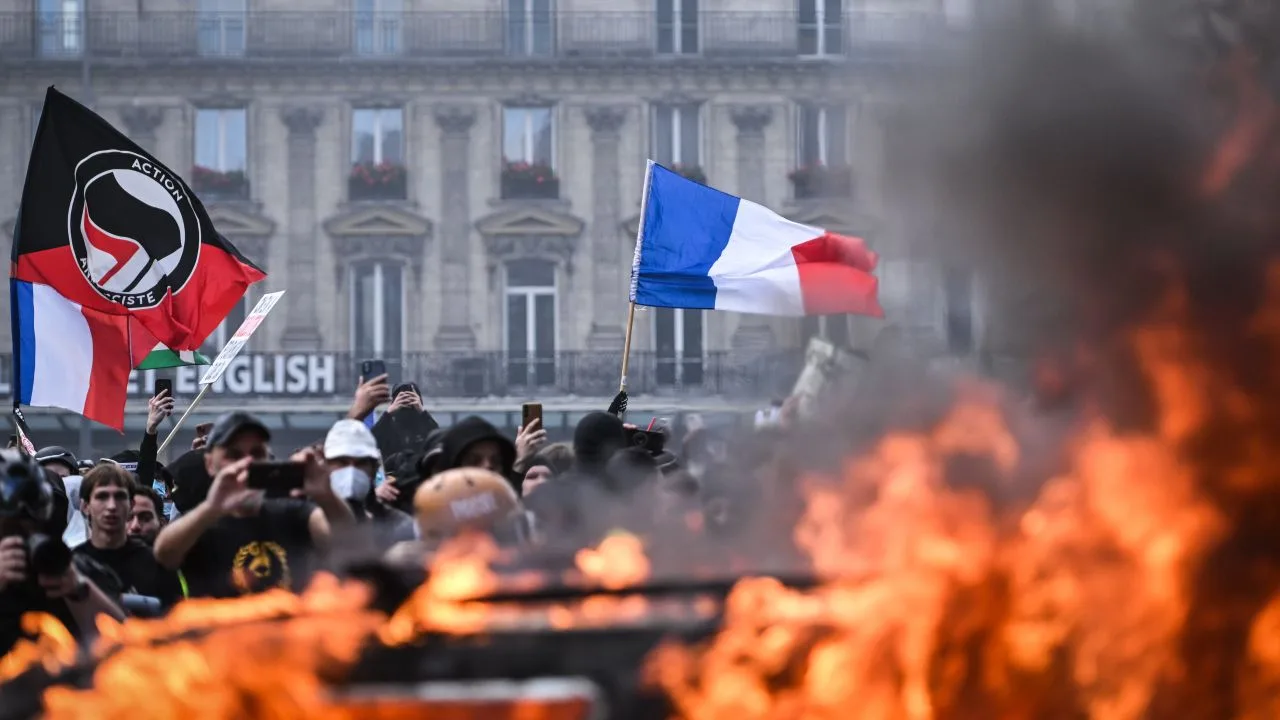 Proteste violente în Franța, cu flăcări și steaguri în fundal.
