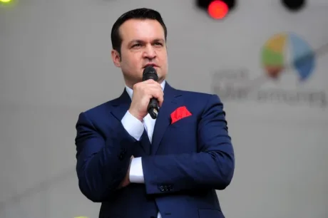 Cătălin Cherecheș vorbește la microfon, îmbrăcat elegant.