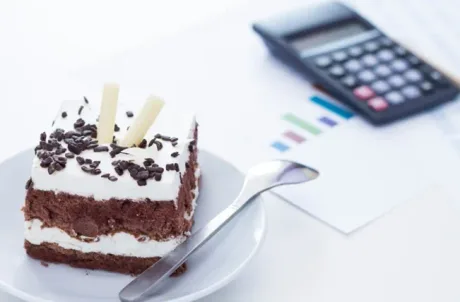 Prăjitură delicioasă pe farfurie, alături de un calculator și documente.
