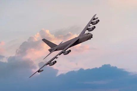 Avion militar zburând pe un fundal de cer cu nori roz și portocalii.