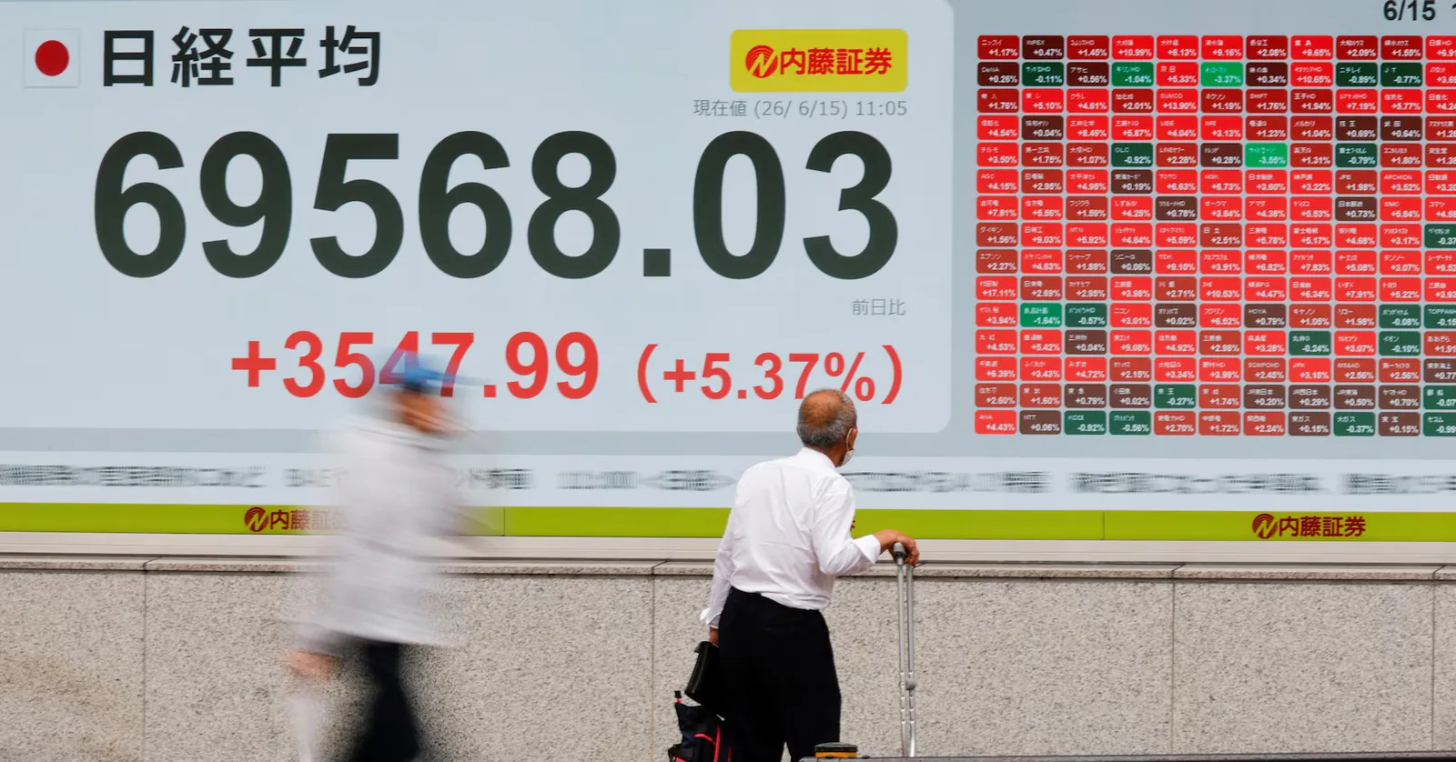 Un bărbat observă un panou cu date financiare pe o stradă aglomerată din Asia.