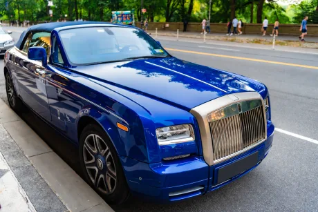 Un Rolls-Royce albastru parcat pe o stradă, înconjurat de vegetație și oameni.