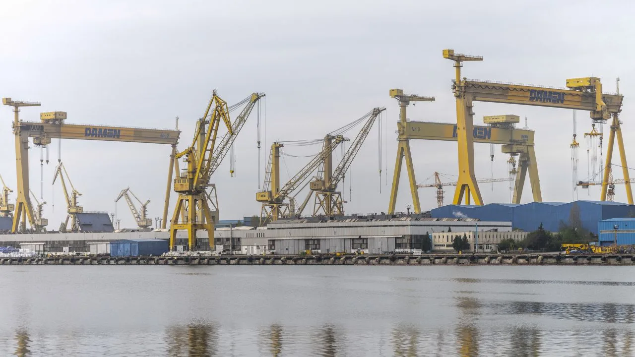Șantierul naval Damen Mangalia, cu macarale și clădiri, pe malul apei.