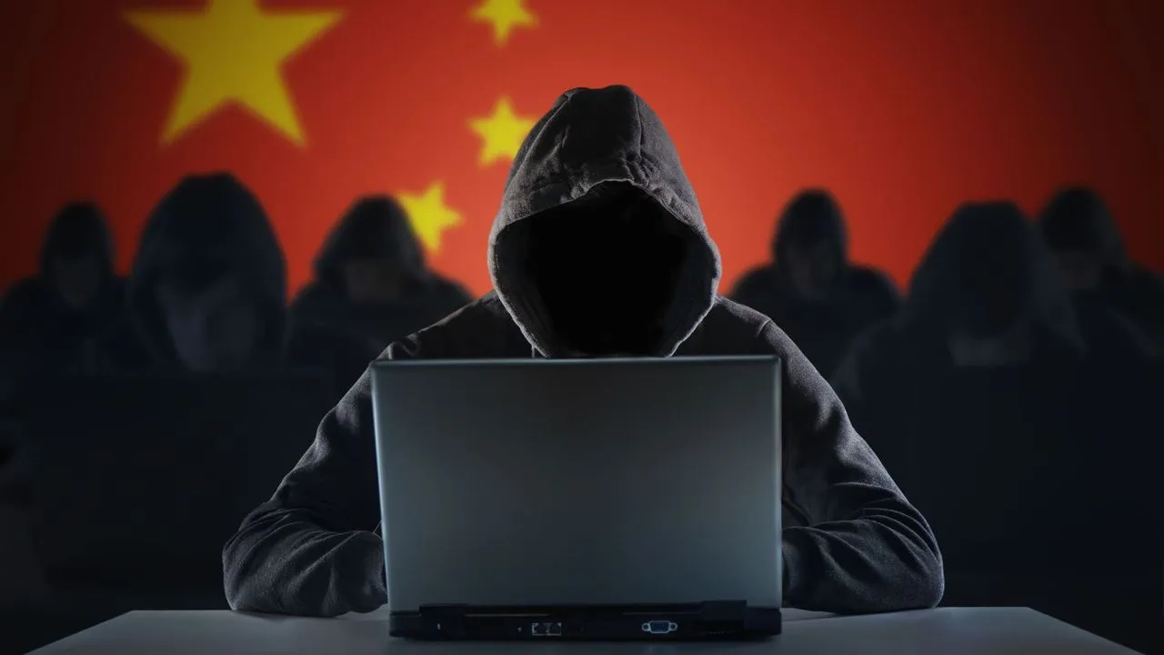 Hacker la laptop, cu steagul Chinei în fundal, simbolizând atacuri cibernetice.