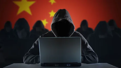 Hacker la laptop, cu steagul Chinei în fundal, simbolizând atacuri cibernetice.