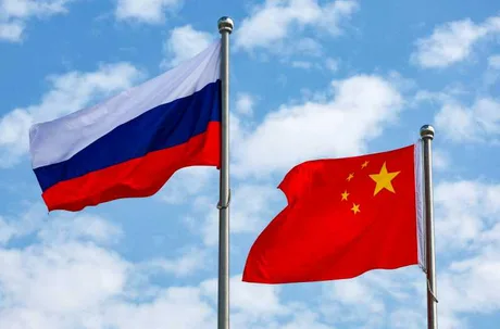 Steagurile Rusiei și Chinei fluturând împreună sub un cer senin.