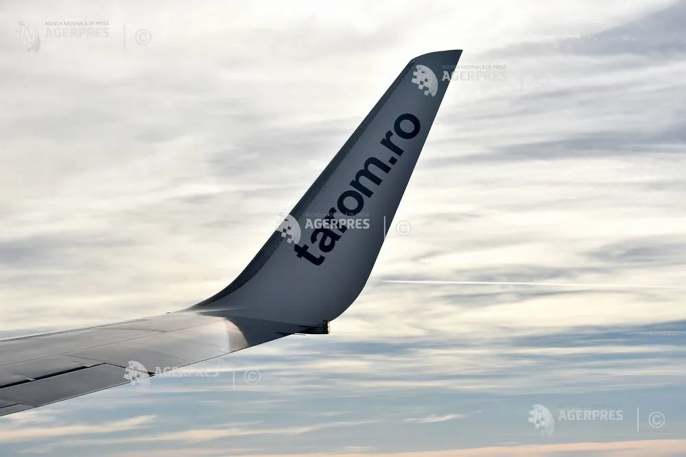 Vârful aripii unui avion TAROM în zbor, cu cer noros în fundal.
