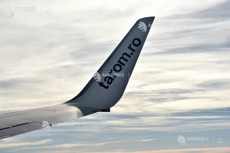 Vârful aripii unui avion TAROM în zbor, cu cer noros în fundal.