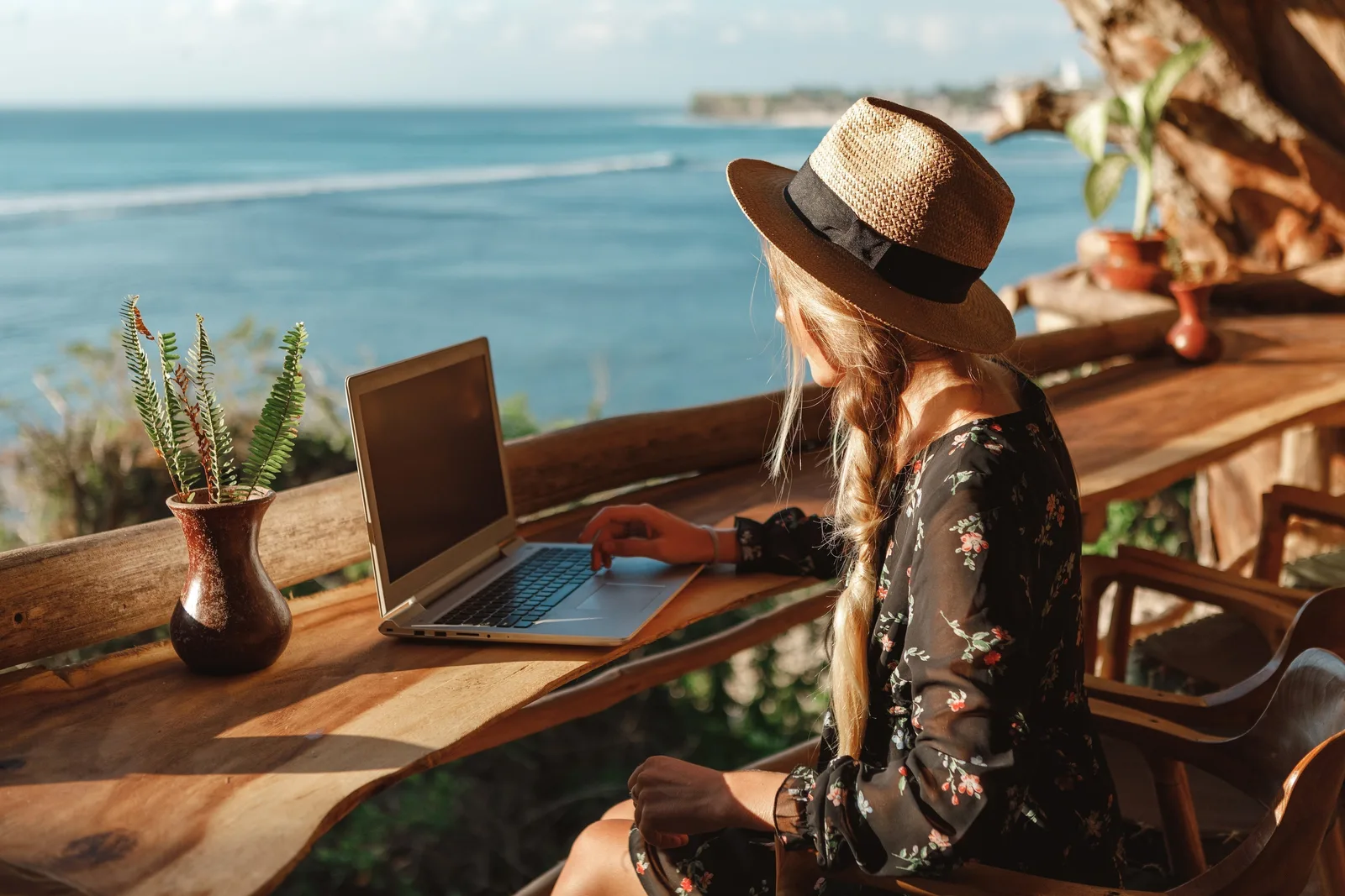 Persoană lucrând la laptop pe o terasă cu vedere la mare.