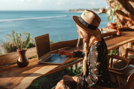 Persoană lucrând la laptop pe o terasă cu vedere la mare.