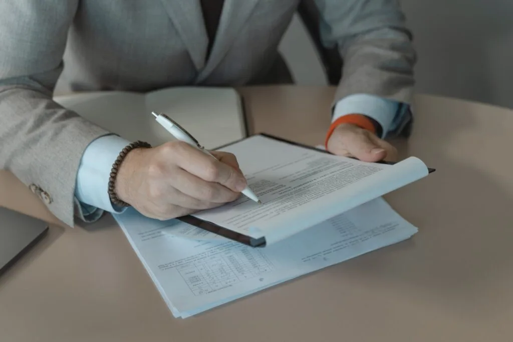 Un bărbat semnează un contract pe birou, cu documente și un pix.
