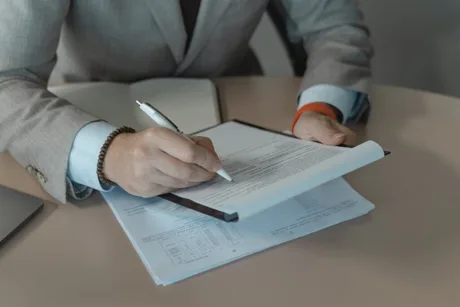 Un bărbat semnează un contract pe birou, cu documente și un pix.