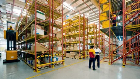 Spațiu de depozitare cu rafturi pline și angajați discutând despre logistică.