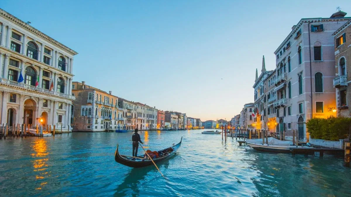 Canale venețiene cu gondole și clădiri istorice la apus.