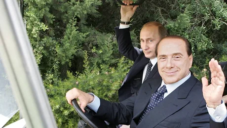Hamad bin Jassim și Silvio Berlusconi într-o mașină, zâmbind și salutând.