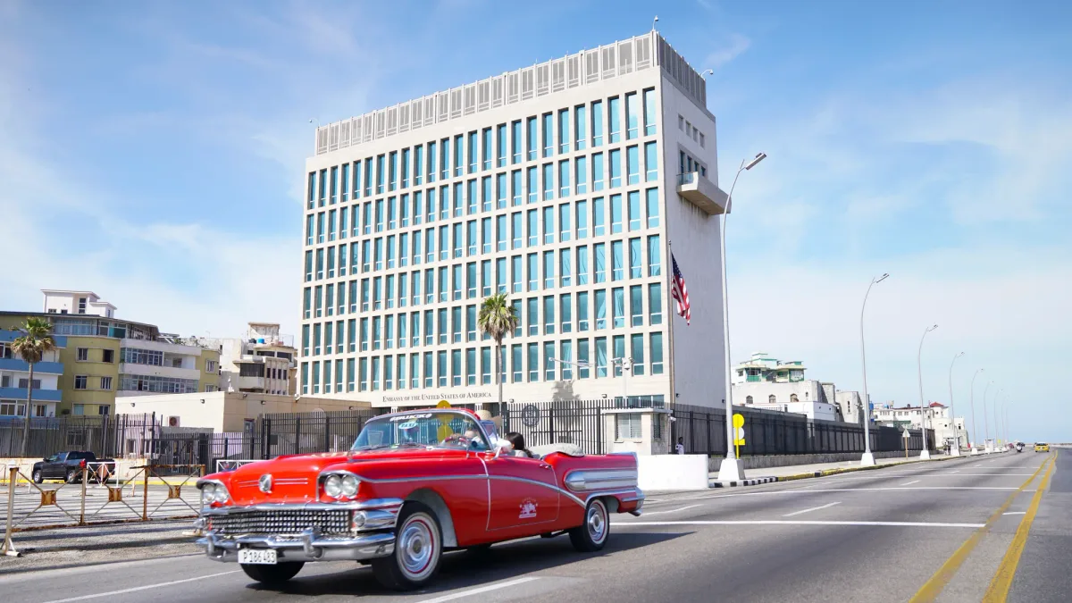 Un automobil clasic roșu trece pe lângă o clădire emblematică din Havana.