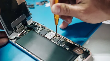 Un tehnician repară un smartphone, lucrând la componentele interne ale acestuia.