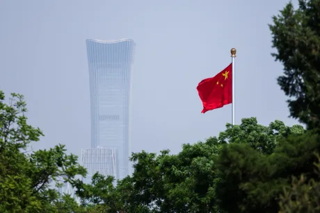 Steag chinezesc fluturând în fața zgârie-norului CITIC Tower din Beijing.